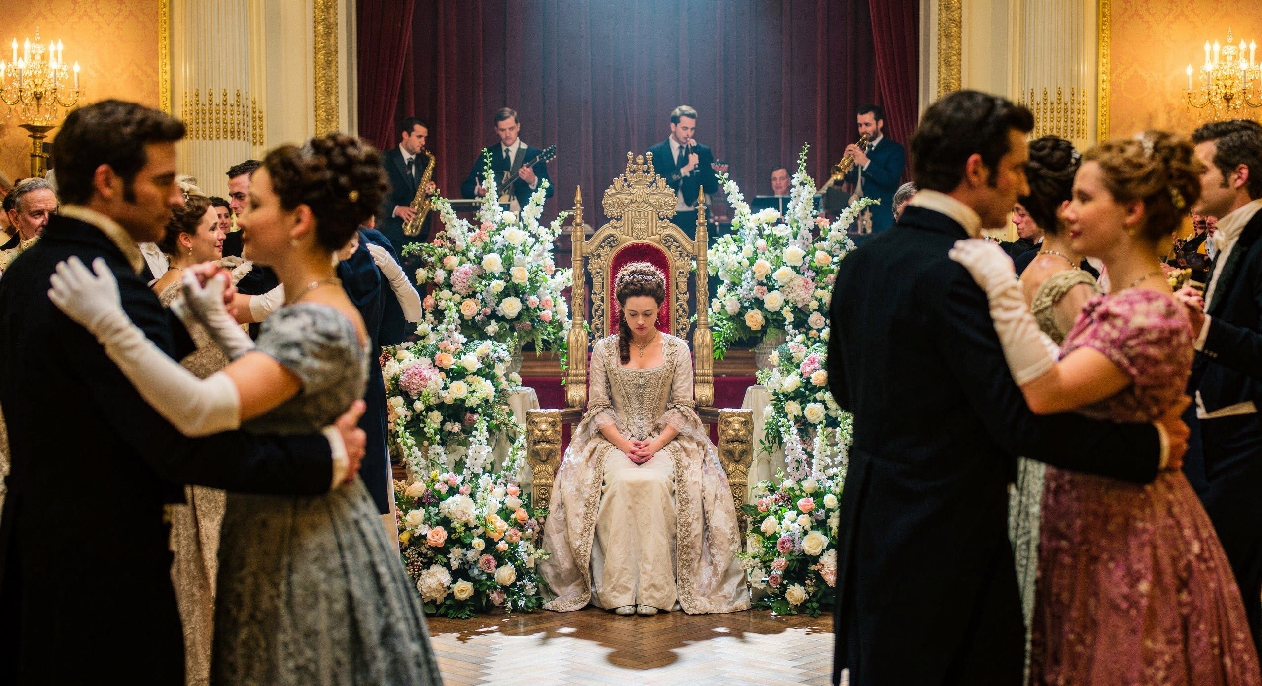 Une jeune femme en robe d'époque assise seule sur un trône doré lors d'un bal majestueux, entourée de couples qui dansent et de compositions florales luxuriantes. Intimité avec Dieu.