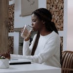 A woman works from her home office on a laptop while drinking water, creating a modern, productive atmosphere.