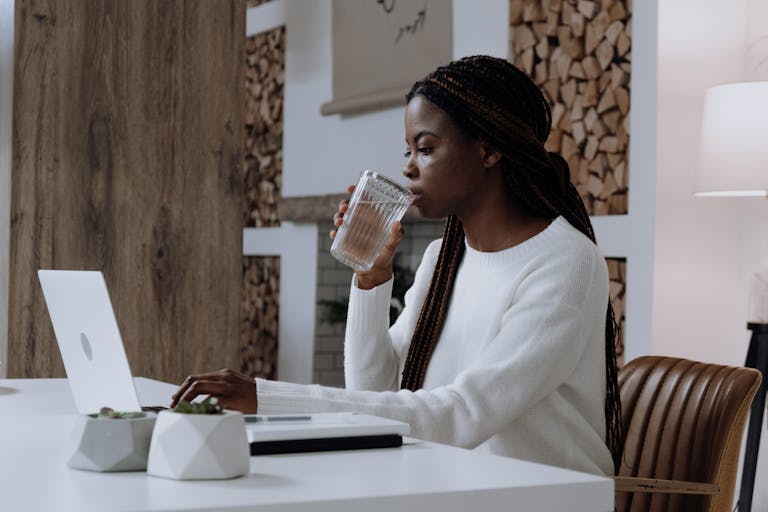 A woman works from her home office on a laptop while drinking water, creating a modern, productive atmosphere.