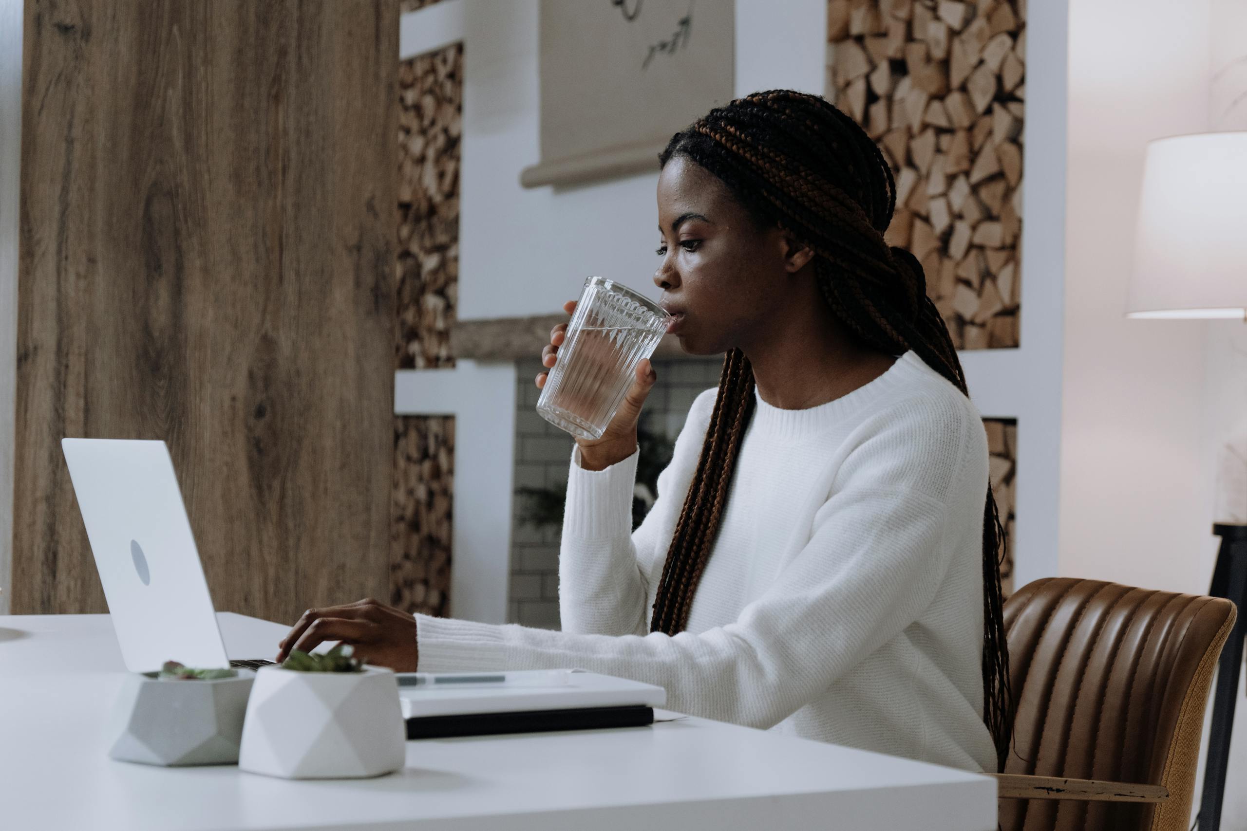 A woman works from her home office on a laptop while drinking water, creating a modern, productive atmosphere.