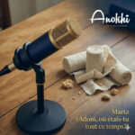 Microphone de studio bleu et or à côté de bandes de lin enroulées (bandelettes funéraires) sur une table en bois. Le texte indique « Marta (Adoni, où étais-tu tout ce temps?) ».