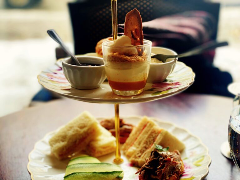 Présentoir de service à deux étages garni de sandwichs et de verrines sucrées sur une table. Le tout évoque un festin raffiné.