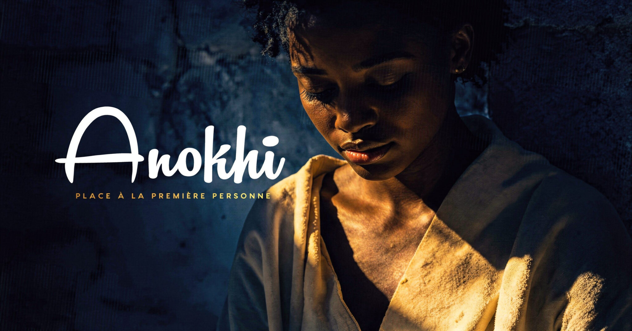 Portrait d'une femme noire, les yeux fermés et la tête baissée, son visage et son épaule éclairés par une lumière dorée latérale qui contraste avec les ombres bleu nuit profondes d'un mur de pierre en arrière-plan.