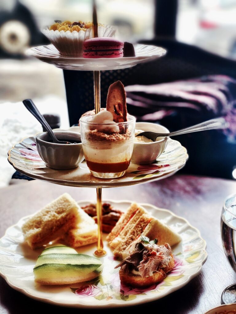 Présentoir de service à trois étages garni de sandwichs et de verrines sucrées sur une table. Le tout évoque un festin raffiné.