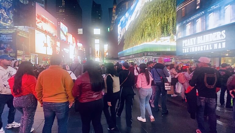 Une foule dense vue de dos à Times Square, New York, la nuit, entourée de panneaux d'affichage lumineux colorés. Une allégorie visuelle de la multitude étouffante dans laquelle la femme à la perte de sang a dû se faufiler.